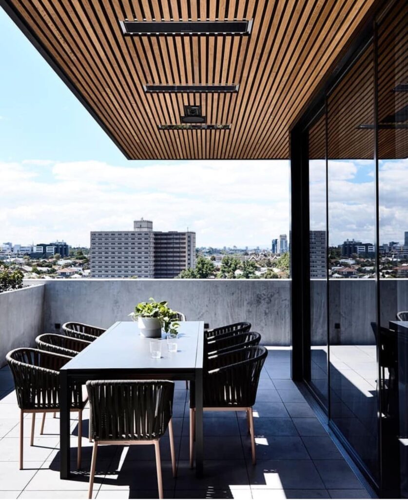 Grey tiled balcony with table and wooden slatted ceiling featuring recessed black heaters