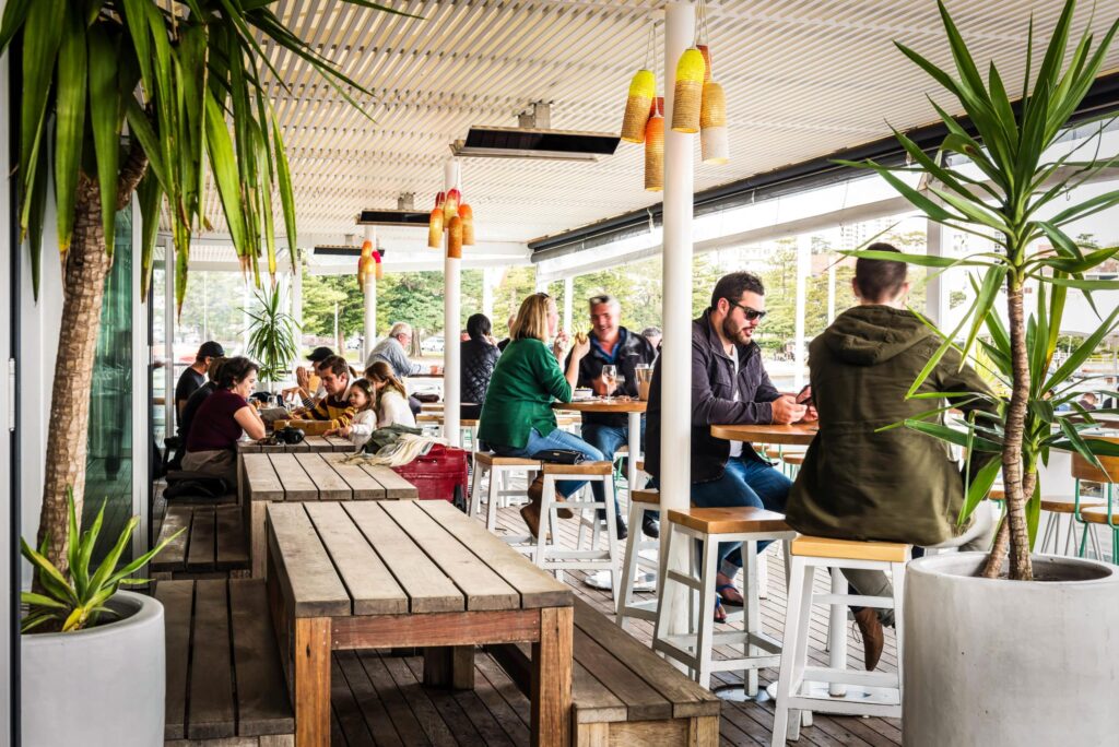 Busy outdoor bar and dining area with potted plants in the foreground and electric heating