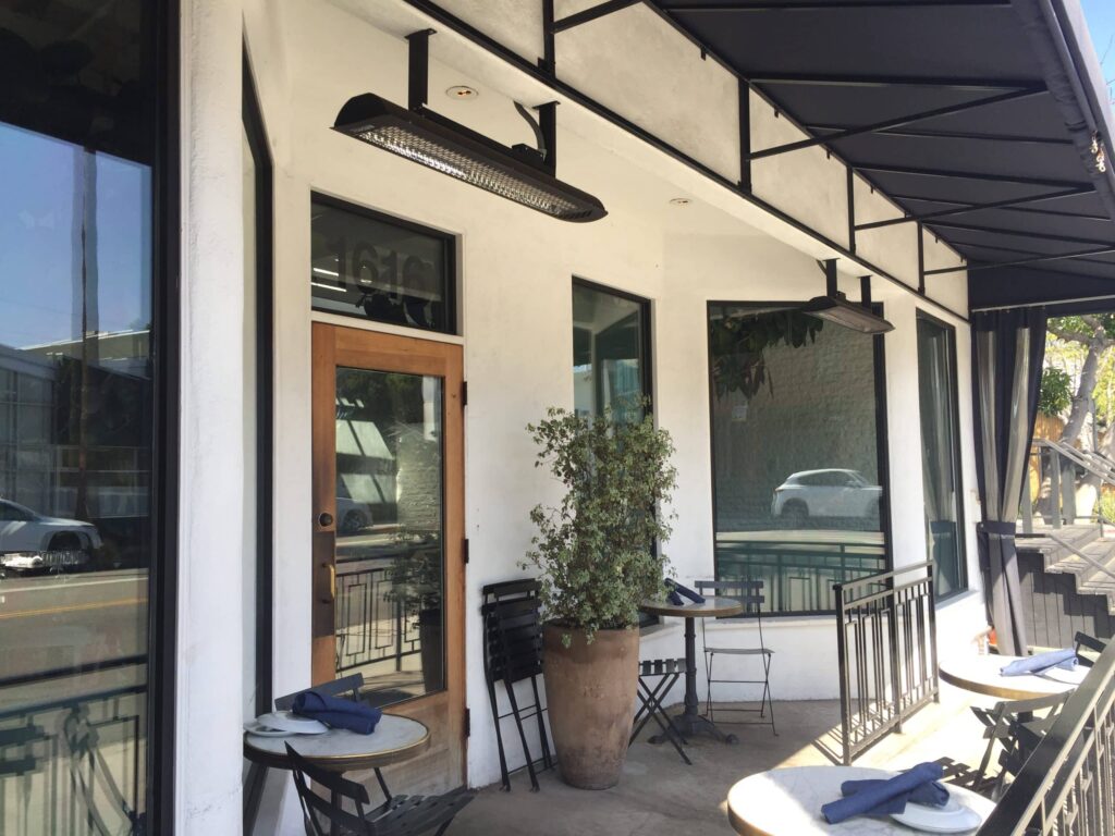 Cafe entrance with small two seater tables and heater hanging above door
